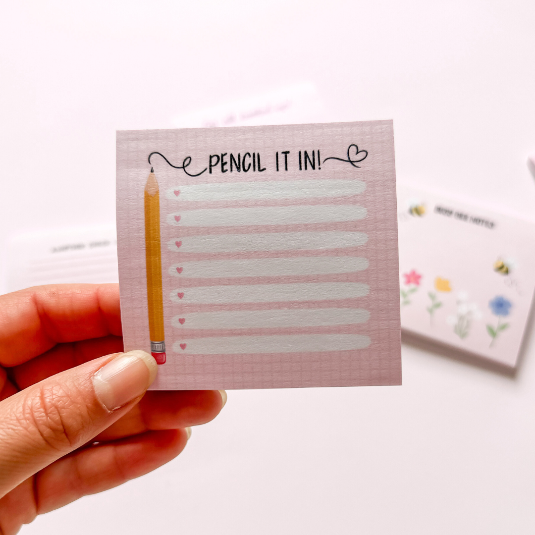 Hand-illustrated pink sticky notepad with a pencil design on a checkered background, featuring rows of lines for writing, labeled 'Pencil It In.