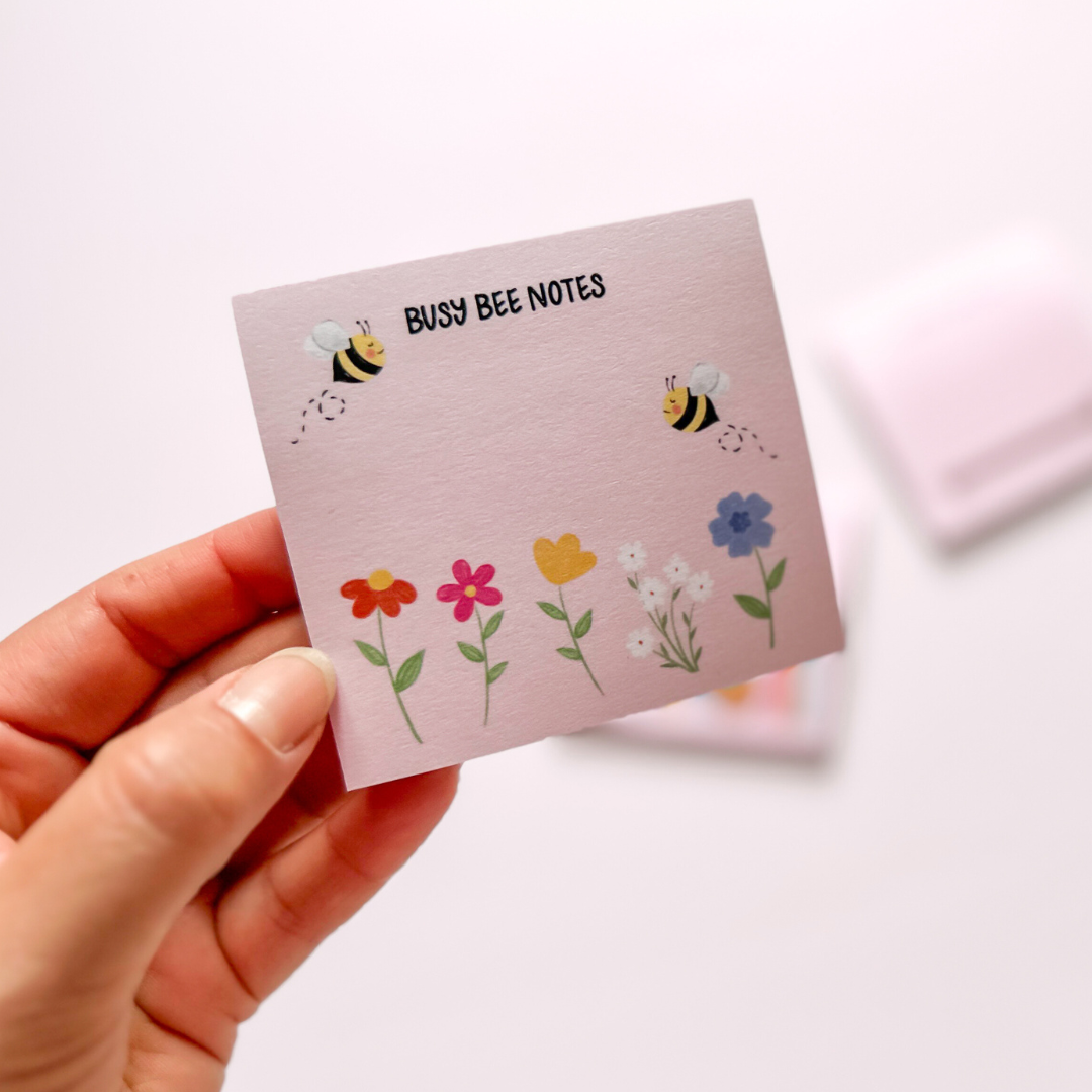 Hand-illustrated pink sticky notepad adorned with bumble bees and flowers, featuring the label 'Busy Bee Notes'.