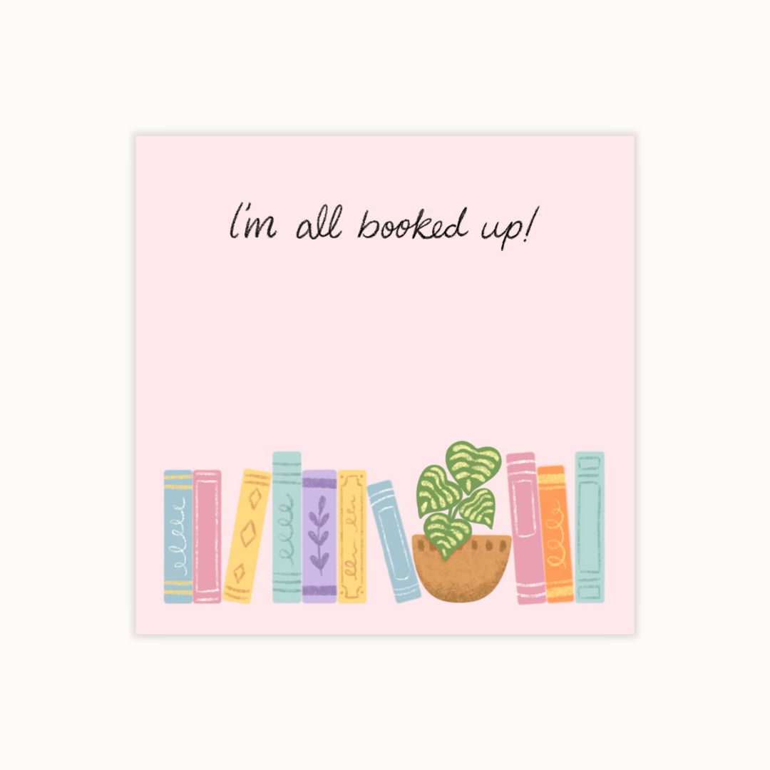 Hand-illustrated pink sticky notepad featuring a row of colorful books and a potted plant, with the label 'I'm All Booked Up'.